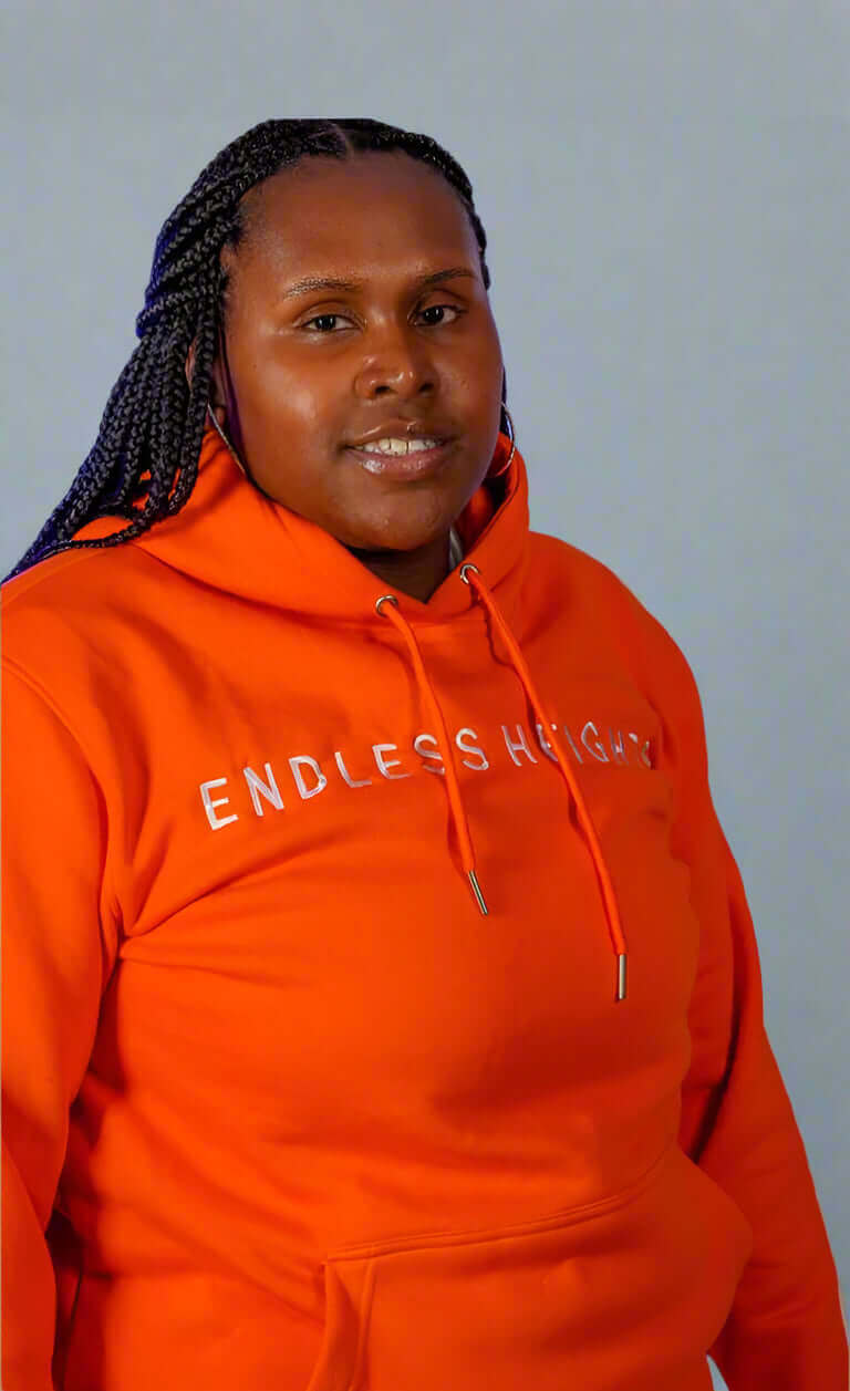 Model wearing an orange hoodie from the Taller Than LIfe Collection with text 'ENDLESS HEIGHTS'