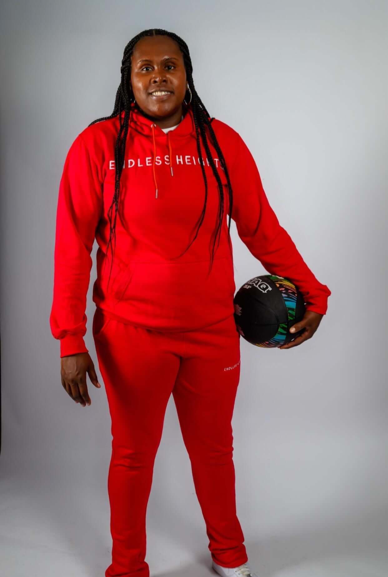 Model wearing a red Sky High Stacked jogging set, holding a colorful basketball, showcasing Endless Heights style.
