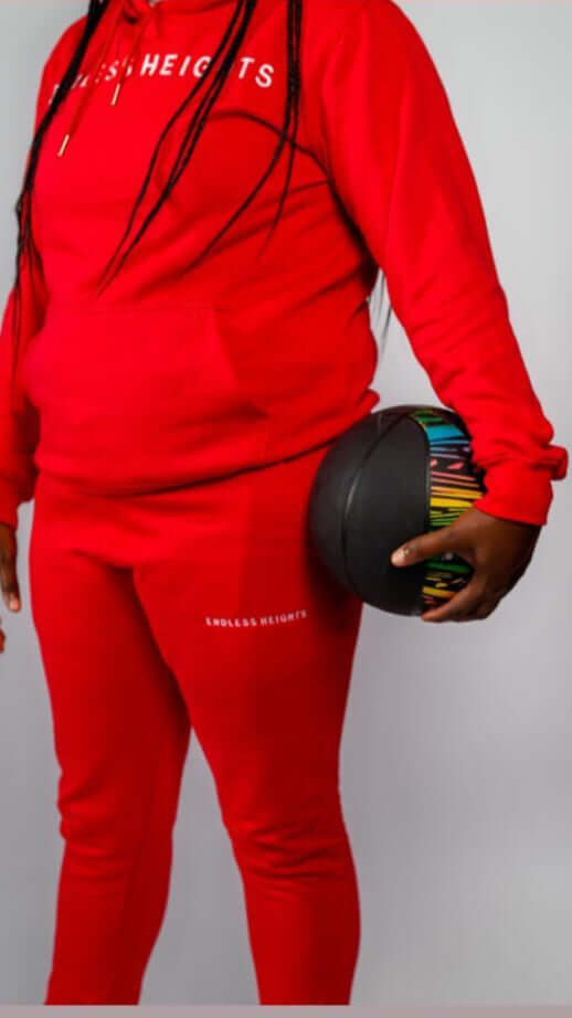 Sky High Stacked Jogging Set in red featuring Endless Heights logo, held by a person with a colorful ball.