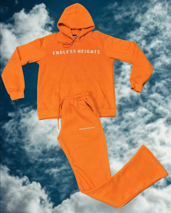 Sky High Stacked Jogging Sets in orange featuring ENDLESS HEIGHTS, set against a cloudy blue background.