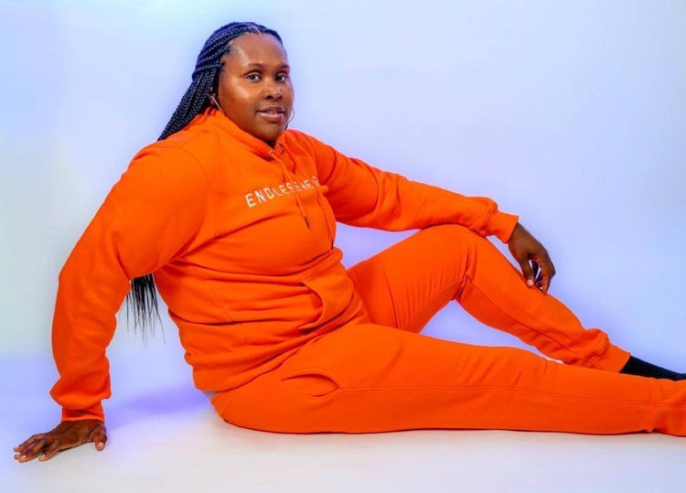 Person wearing bright orange tracksuit from the Taller Than LIfe Collection, showcasing casual and trendy fashion.