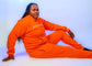 Person wearing bright orange tracksuit from the Taller Than LIfe Collection, showcasing casual and trendy fashion.