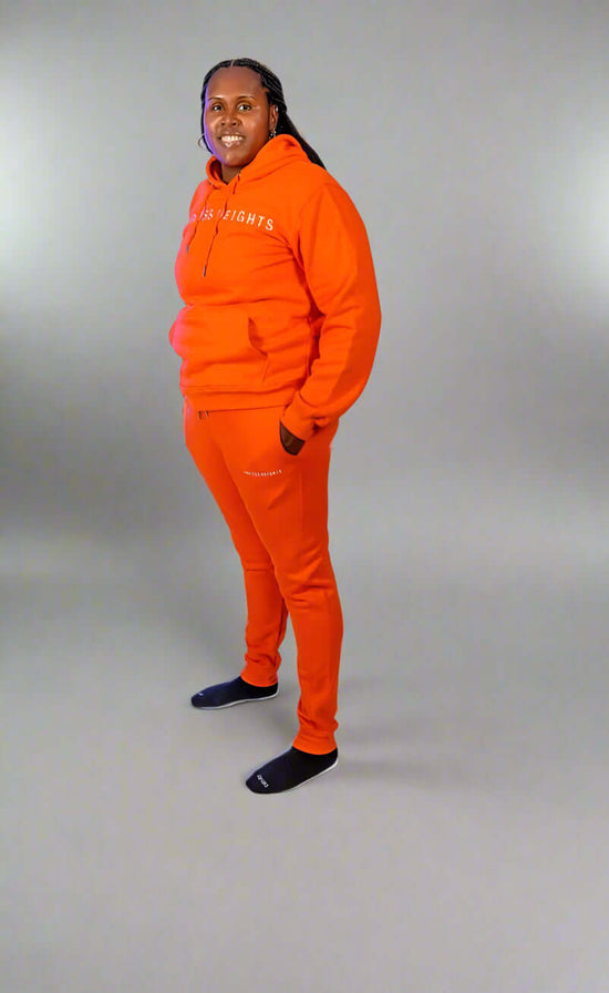 Person wearing an orange hoodie and matching sweatpants from the Taller Than LIfe Collection, posing confidently.