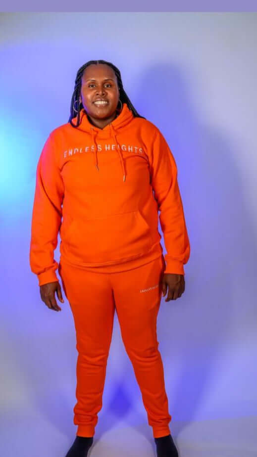 Model wearing the Taller Than LIfe Collection in bright orange hoodie and sweatpants.