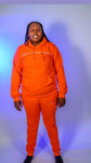 Model wearing the Taller Than LIfe Collection in bright orange hoodie and sweatpants.