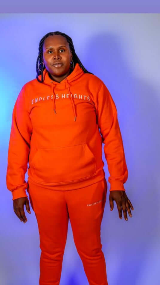 Taller Than LIfe Collection model wearing ENDLESS HEIGHTS tracksuit set in vibrant orange hoodie and matching pants.
