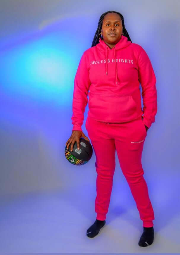 Model wearing ENDLESS HEIGHTS tracksuit from Taller Than LIfe Collection, holding a basketball against a blue backdrop.