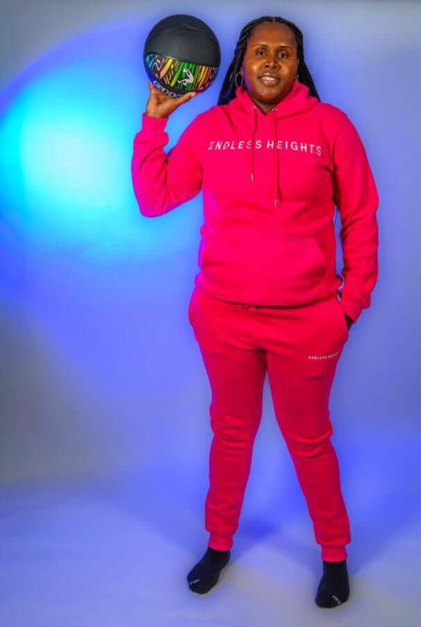 Model showcasing the Taller Than LIfe Collection in a vibrant pink ENDLESS HEIGHTS tracksuit with a basketball.